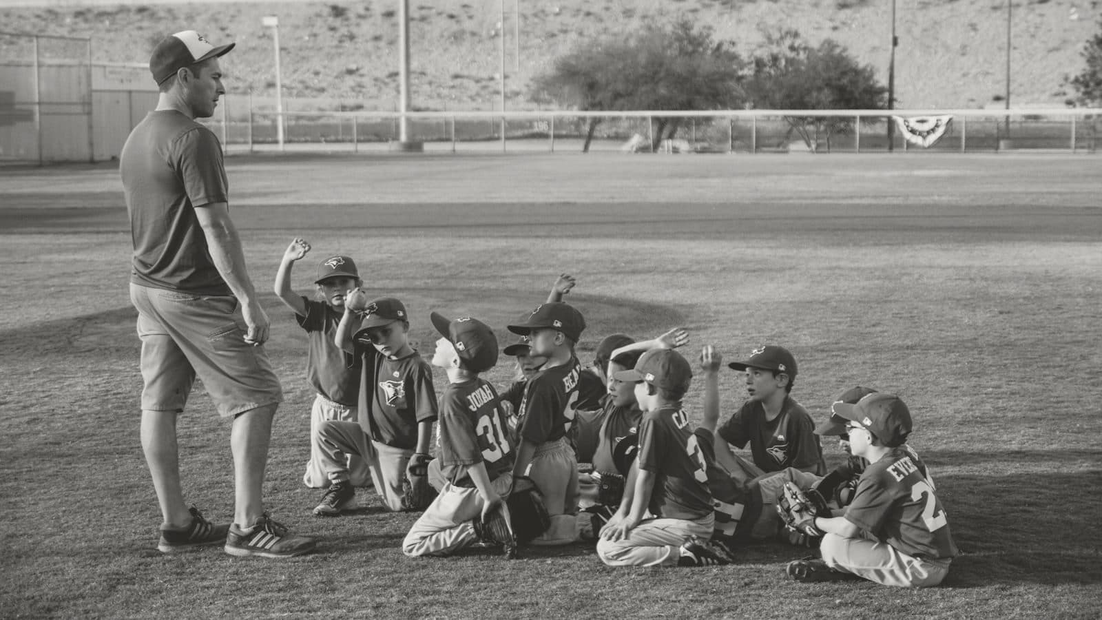 A coach huddles with a youth baseball team on the field